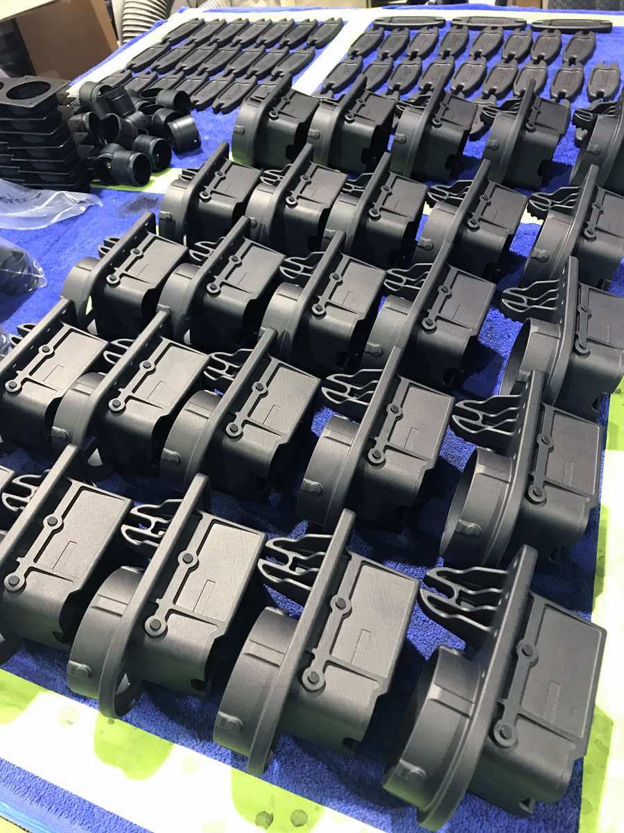 Rows of identical black plastic components are neatly arranged on a blue cloth, likely for inspection or assembly—highlighting Ohio’s Manufacturing Strength in producing detailed mechanical or electronic housing pieces.