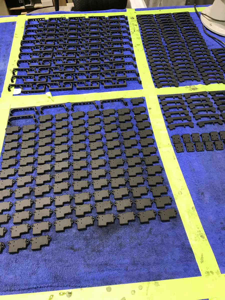 Numerous small black plastic parts are neatly arranged in rows on a blue surface divided by yellow tape, showcasing organized sorting or assembly—reflecting the precision and efficiency often seen in Ohio manufacturing settings.